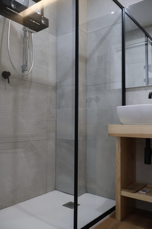 Bagno moderno nelle Tage Rooms di Catania con cabina doccia in vetro, lavabo bianco su vanity in legno e piastrelle grigie