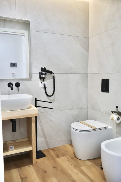 Bagno moderno in Taga Rooms Catania con sanitari in ceramica bianca, piastrelle in marmo, mobile in legno e dettagli neri