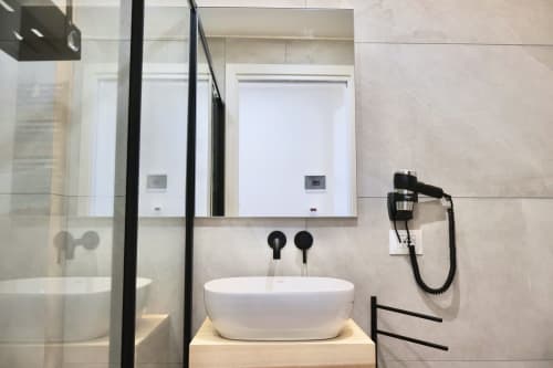 Bagno moderno in Taga Rooms Catania con lavabo bianco a ciotola, rubinetteria nera, specchiere e doccia