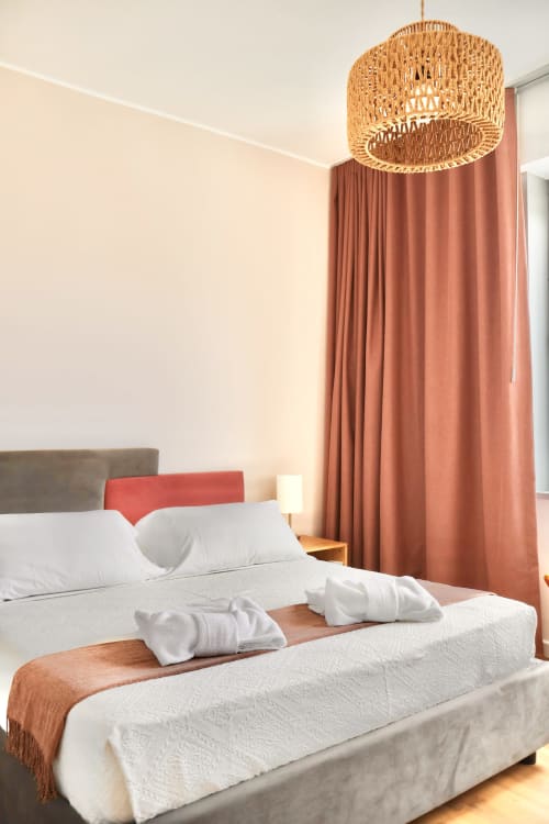 Camera moderna di Taga Rooms Catania con letto queen, lampada a sospensione intrecciata, tende color terracotta e vista sulla città