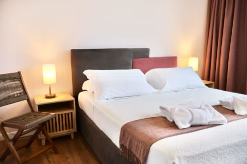 Camera moderna al Taga Rooms di Catania con biancheria bianca, testata scura, cuscini decorativi e illuminazione calda dai comodini