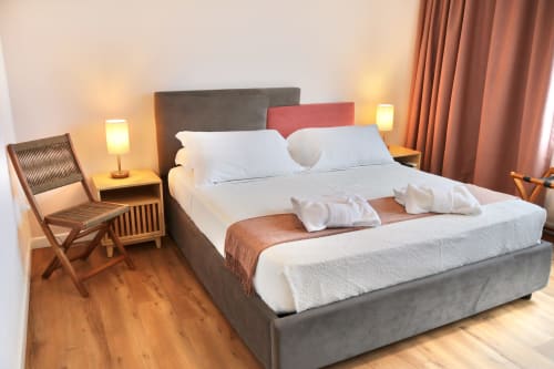 Camera moderna a Taga Rooms Catania con letto imbottito grigio, biancheria bianca, illuminazione calda, pavimenti in legno e vista sulla città