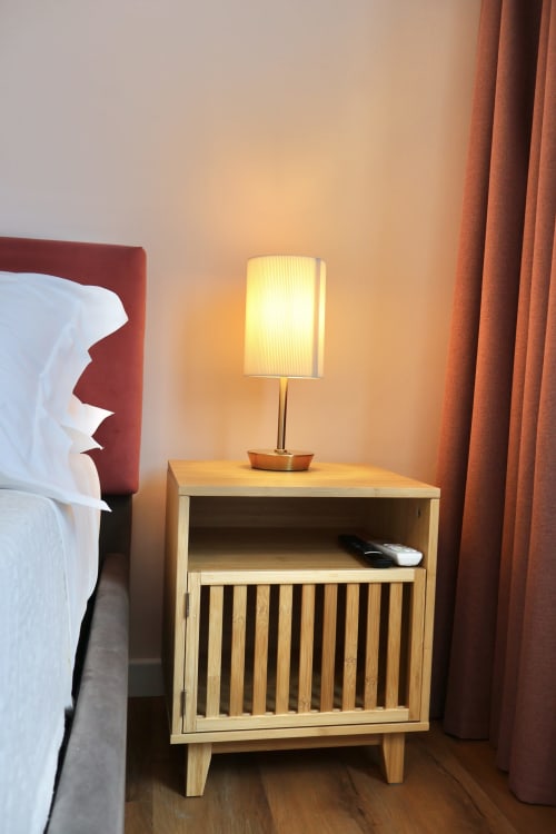 Comodino in legno con lampada illuminata nella camera da letto dell'hotel Taga Rooms Catania, design minimale moderno