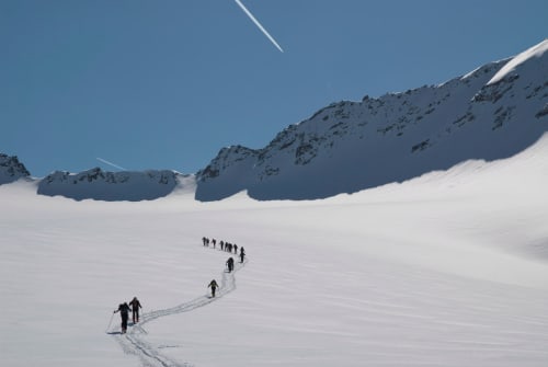 Groupe de skieurs en randonnée sur un glacier enneigé près de Calacuccia, Corse, avec montagnes enneigées et ciel bleu dégagé.