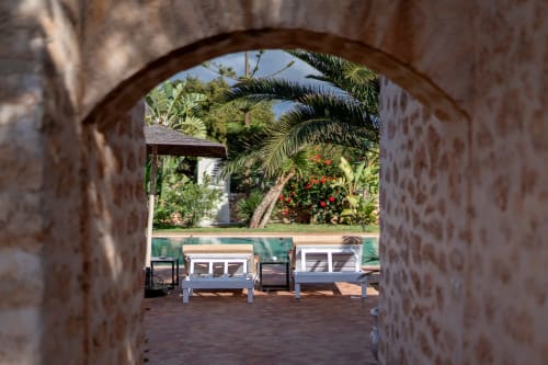 Arched stone passage at Domaine Belhazar opening to pool area with white loungers and tropical garden, Essaouira