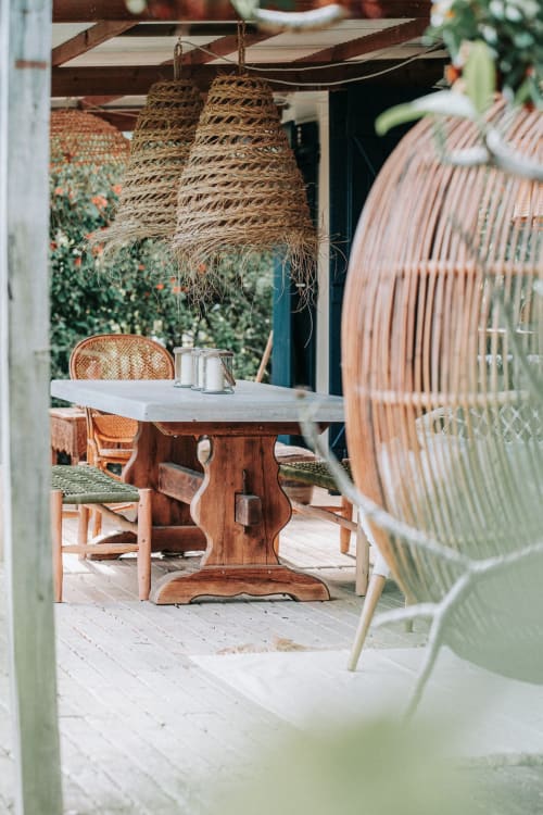 Terrasse rustique à Bleu Guesthouse en France avec luminaires suspendus tissés, table en bois, chaises en rotin et murs couverts de lierre