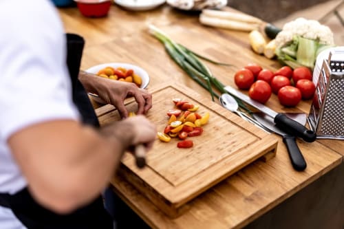 Chef préparant des légumes frais à la cuisine de la Bleu Guesthouse, coupant poivrons et tomates sur planche en bois