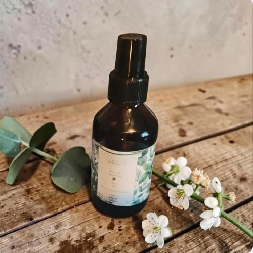 Flacon en verre teinté avec vaporisateur entouré de fleurs blanches et d'eucalyptus sur surface en bois aux Gîtes de Petrocoriis