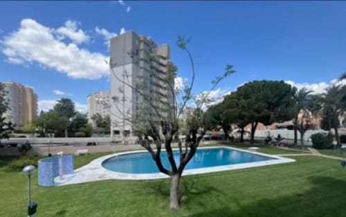 Complejo residencial ROILA360 Alicante con piscina curva, jardín bien cuidado y edificios altos bajo cielo azul