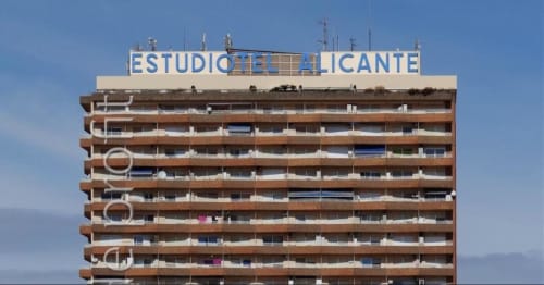 Fachada del edificio de apartamentos Estudios de Alicante en Alicante, España con cielo azul y balcones