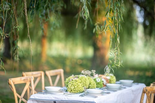 Outdoor garden dining setup at Domaine De Bafave with place settings, green hydrangeas, and willow branches overhead in