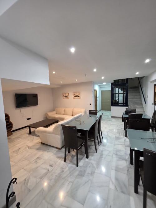 Moderna sala de estar y comedor de planta abierta en Hostal El Pasaje en Puente Genil con suelos de mármol, sofá crema y comedor negro