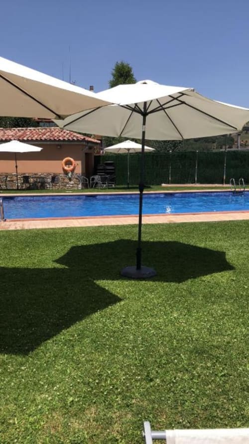 Área de piscina de Casa Tapiolas en Molló con sombrillas, césped verde y piscina azul en día soleado