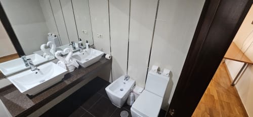 Modern hotel bathroom at Hostal El Pasaje with double sinks, toilets, and white towels on dark tile flooring