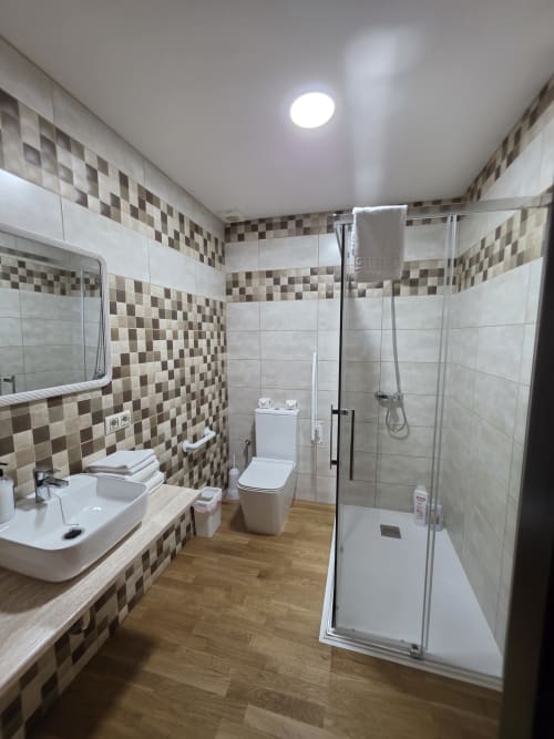 Baño moderno del Hostal El Pasaje en Puente Genil con azulejos a cuadros, ducha de cristal, lavamanos, inodoro y madera