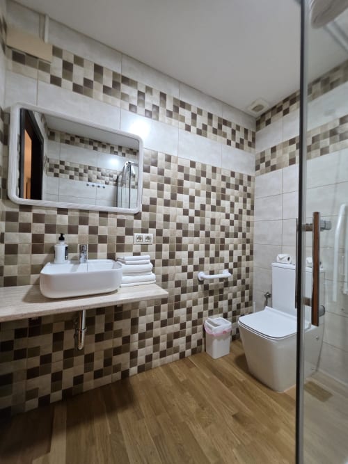 Baño moderno en Hostal El Pasaje, Puente Genil, con paredes de azulejos a cuadros, lavabo blanco, inodoro y piso de madera.