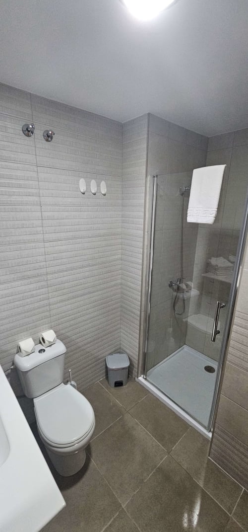 Baño moderno en el Hostal El Pasaje con ducha de cristal, inodoro blanco, lavabo y piso de cerámica