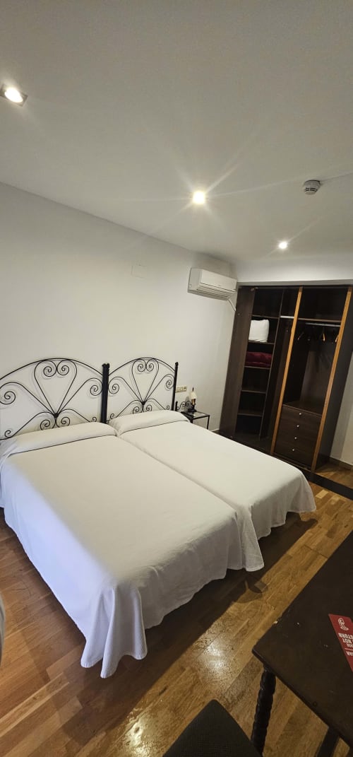 Habitación doble con dos camas individuales, cabeceros de hierro forjado, aire acondicionado, armario y piso de madera en Hostal El