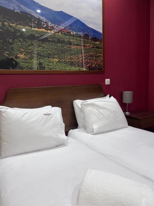 Duas camas com lençol branco em quarto borgonha na Tranca da Barriga, Covilhã, com arte de paisagem montanhosa acima da cabeceira