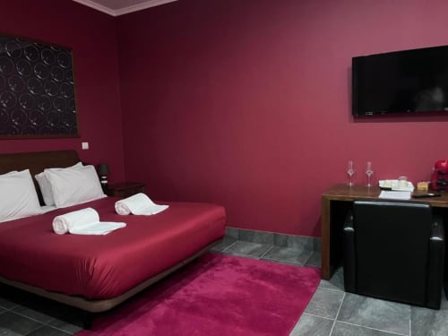 Quarto moderno com paredes rosa, cama queen com almofadas brancas, TV de tela plana, piso de azulejo escuro e tapete bordô