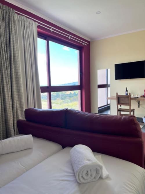 Quarto moderno com sofá bordô, vista para a serra através de grandes janelas e roupa de cama branca na Tranca da Barriga em Covilhã