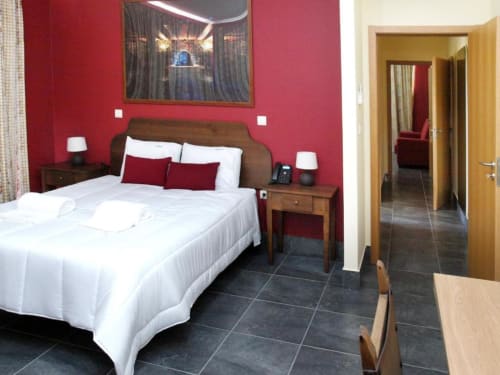 Quarto moderno do hotel Tranca da Barriga com paredes vermelhas, cama branca, móveis de madeira e piso de azulejo escuro em Covilhã.