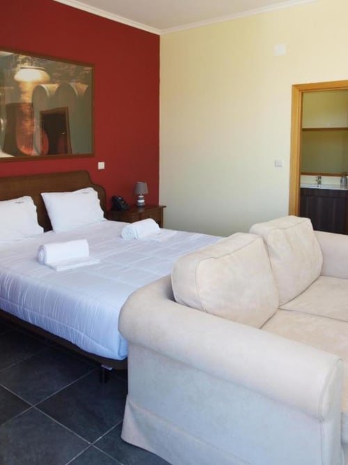 Quarto moderno na Tranca da Barriga com parede de destaque em vermelho, cama de casal, sofá branco e vistas para o jardim em Covilhã