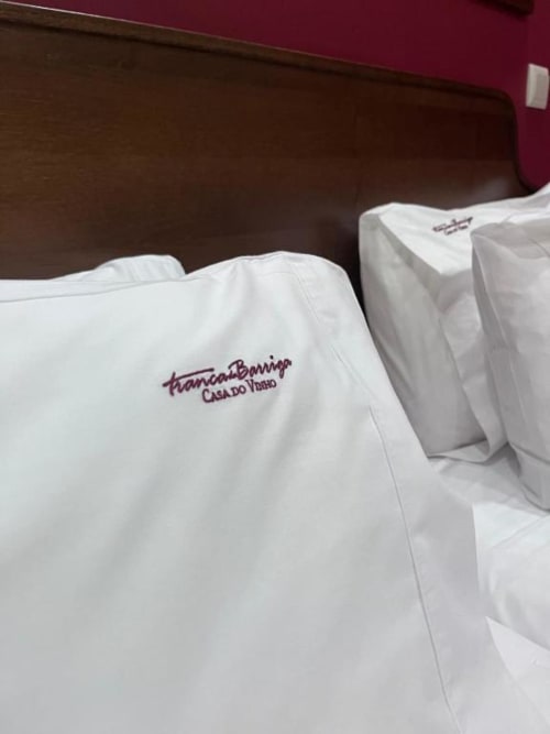 Almofadas brancas com logotipo bordado da Tranca da Barriga Casa do Vinho em cama da pousada em Covilhã