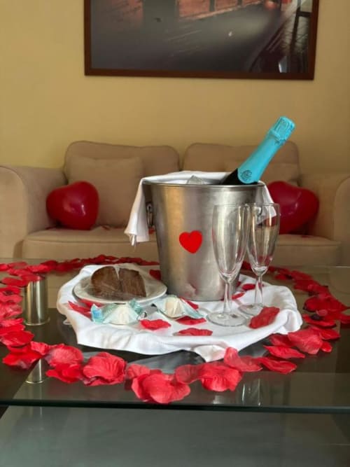 Decoração romântica em Tranca da Barriga com champanhe, bolo de chocolate, pétalas de rosa e taças sobre mesa preta