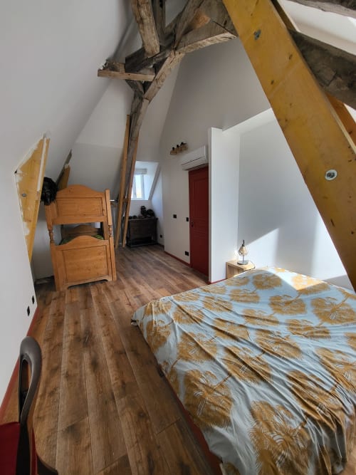Chambre mansardée au Domaine des Oiseaux avec poutres en bois, lit aux draps motifs et parquet