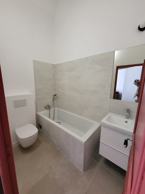 Salle de bain moderne en L au gîte Domaine des Oiseaux de Passage : baignoire, lavabo, toilettes et carrelage beige