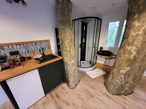 Salle de bain moderne en cabane perchée avec vanité en bois, lavabo noir, douche incurvée et colonnes d'arbres rustiques au Domaine des Oiseaux de