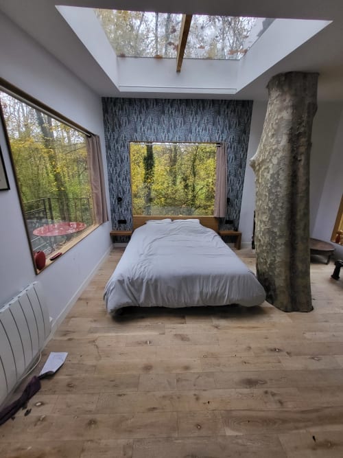 Chambre de cabane moderne au Domaine des Oiseaux de Passage avec puits de lumière, vues sur la forêt et support de tronc d'arbre naturel.