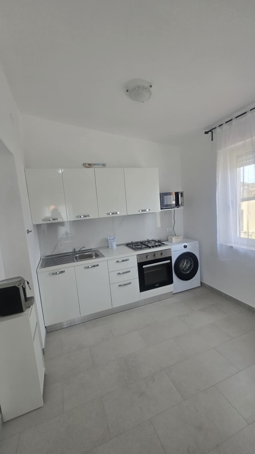 Cucina moderna bianca con piano cottura a gas, forno, lavatrice e lavello nell'appartamento vacanze Tronca