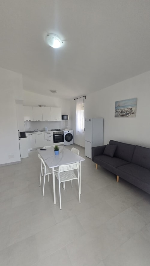 Moderno appartamento open-plan a Tronca con cucina bianca, divano nero, tavolo da pranzo e luminosa plafoniera