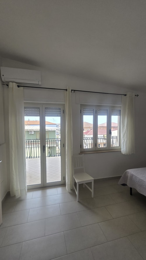 Camera luminosa con porte in vetro che si aprono sulla terrazza con vista sulla costa di Tronca, arredata con biancheria bianca e climatizzatore