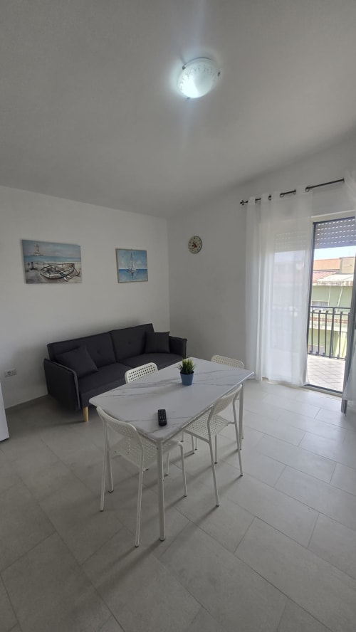 Luminoso soggiorno moderno con divano nero, tavolo bianco e balcone vista mare a Casa Vacanze Maestrale a Tronca