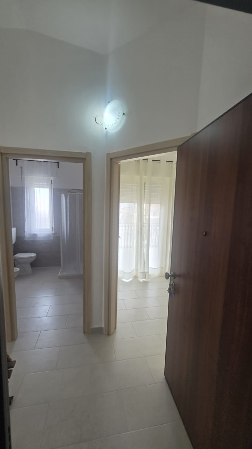 Corridoio moderno con pavimento piastrellato, lampada a soffitto, porta in legno e accessi al bagno e al balcone