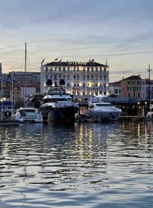 Luxuriöse Yachten in der Hafenanlage des Hotel Splendid Cannes bei Sonnenuntergang mit beleuchteter Belle-Époque-Architektur