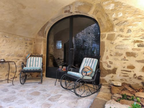 Rustic stone patio at Magnanerie de Sainte Croix with striped chairs and wrought iron furnishings overlooking a garden