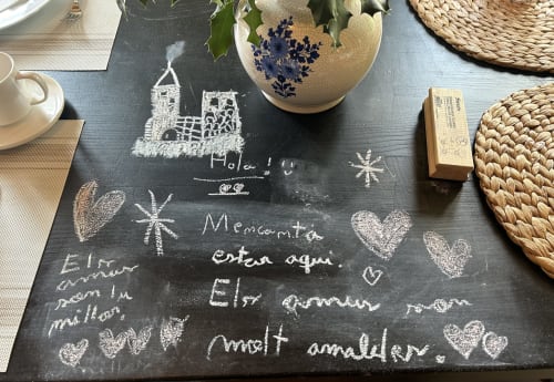 Cartel de bienvenida en pizarra en Casa Tapiolas B&B en Molló, Girona con mensajes manuscritos y corazones decorativos