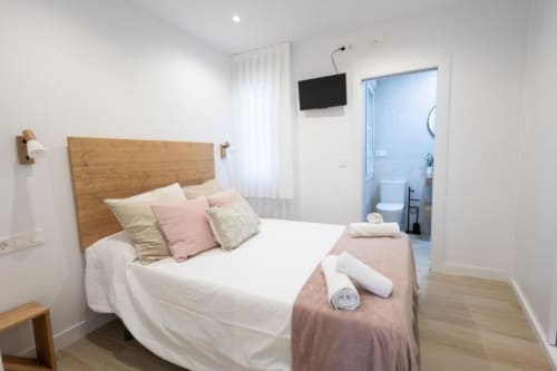 Dormitorio moderno en Apartamentos La Búsqueda, Cuenca, con cabecero de madera, ropa de cama blanca y baño privado visible
