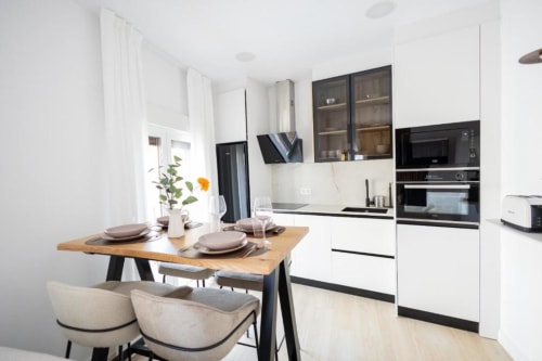 Cocina y comedor moderno en apartamento de Cuenca con muebles blancos, electrodomésticos negros, mesa de madera y vistas a la ciudad