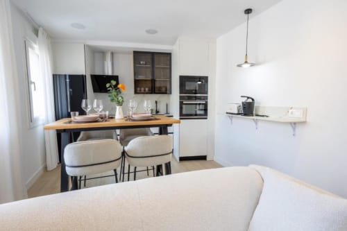 Cocina y comedor moderno en apartamento de Cuenca con encimera de madera, muebles blancos y cómodos asientos