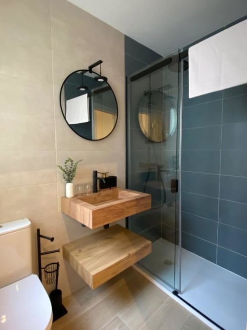 Baño moderno en apartamento de Cuenca con lavabo de madera, espejo redondo, ducha con azulejos verde azulado oscuro e inodoro