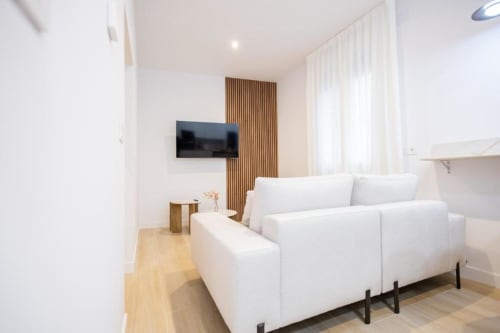 Moderna sala de estar en apartamento de Cuenca con sofá blanco, TV de pantalla plana, pared de acento de madera y luz natural