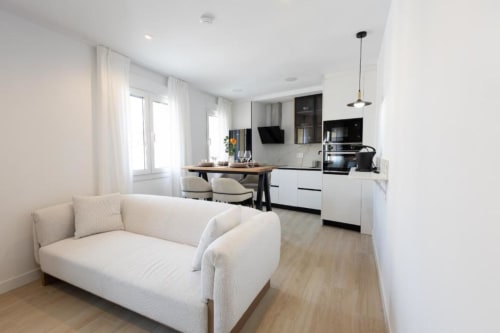Sala de estar moderna y diáfana en apartamento de Cuenca con sofá crema, cocina blanca, comedor y vistas a la ciudad