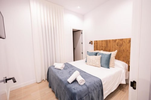Dormitorio moderno en apartamento de Cuenca con cabecero de madera, ropa de cama blanca, detalles azules y piso de madera clara