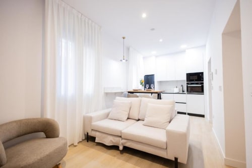 Moderno salón de planta abierta y cocina en apartamento de Cuenca con sofá crema, comedor y cocina equipada