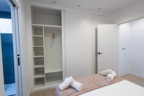 Dormitorio moderno en apartamento de Cuenca con armario empotrado, puertas blancas, suelo de madera y toallas enrolladas en la cama